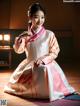 A woman in a pink and white hanbok sitting on the floor.